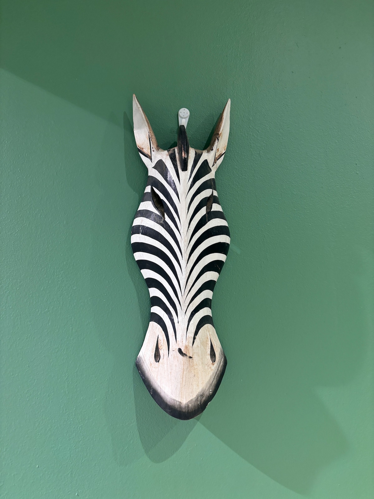 A decorative wooden zebra wall art piece is positioned against a vibrant green wall, featuring distinct black and white stripes. The sculpture is designed to capture attention, adding an artistic touch to the space.