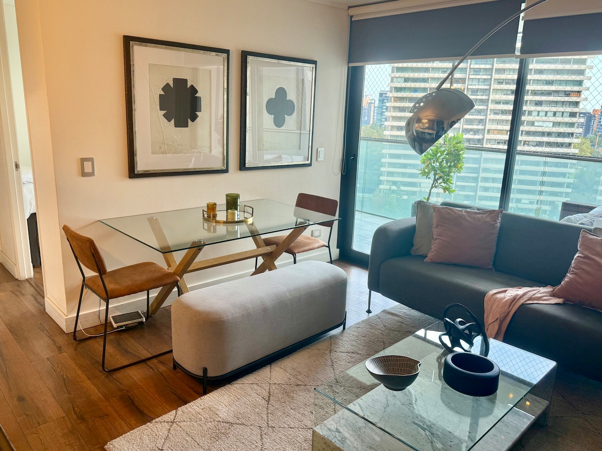 A contemporary living space features a glass dining table with two wooden chairs and a cushioned bench. A plush sofa with accent pillows is positioned next to a coffee table made of glass and stone. Large windows provide natural light and city views.