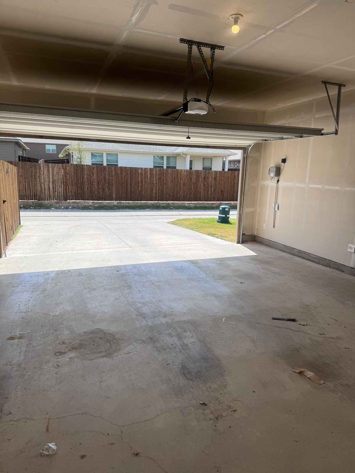 An empty garage is shown with a smooth concrete floor and a large opening faced towards the driveway. Natural light filters in from the open garage door, revealing a tidy space with bare walls and a single overhead light fixture.