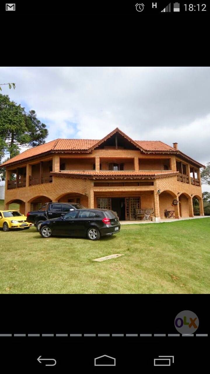 The exterior of a spacious brick house is highlighted, featuring a traditional roof and multiple levels. Large windows and porches are visible, surrounded by a green lawn. Two parked vehicles, a yellow car and a black SUV, are positioned in front of the house.