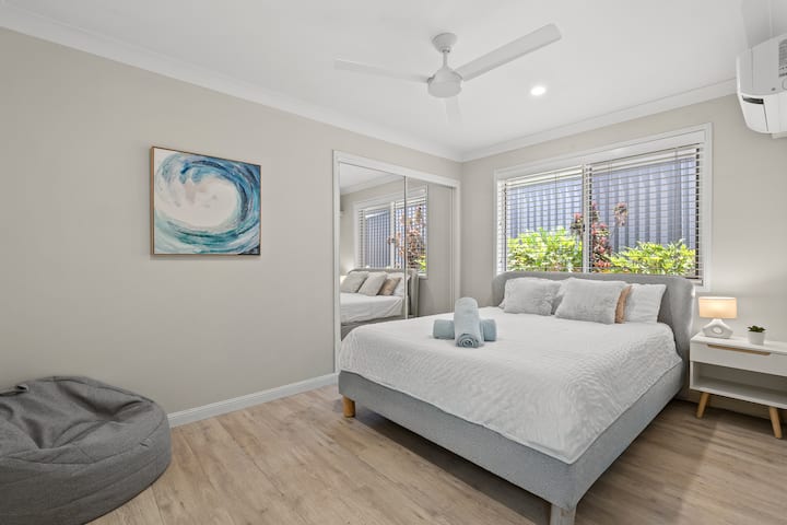 Quarto iluminado com cama queen size e pufe aconchegante para relaxar.