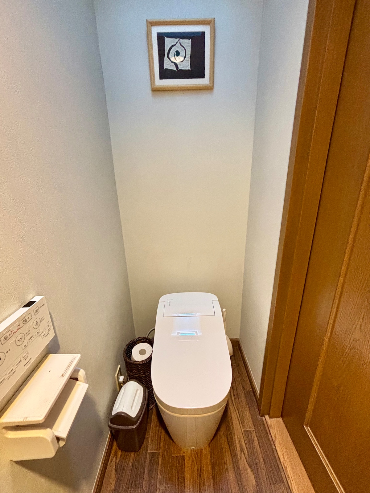 A compact bathroom space features a modern toilet with a sleek design. The walls are painted in soft tones, and a small framed artwork adds a touch of character. A wastebasket is discreetly placed beside the toilet, ensuring convenience.