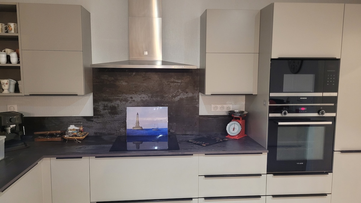 A modern kitchen is presented with sleek gray cabinetry and a polished countertop. Stainless steel appliances, including an oven and a hood, are featured alongside a glossy backsplash. A decorative image sits on the countertop, complementing the functional kitchen workspace.