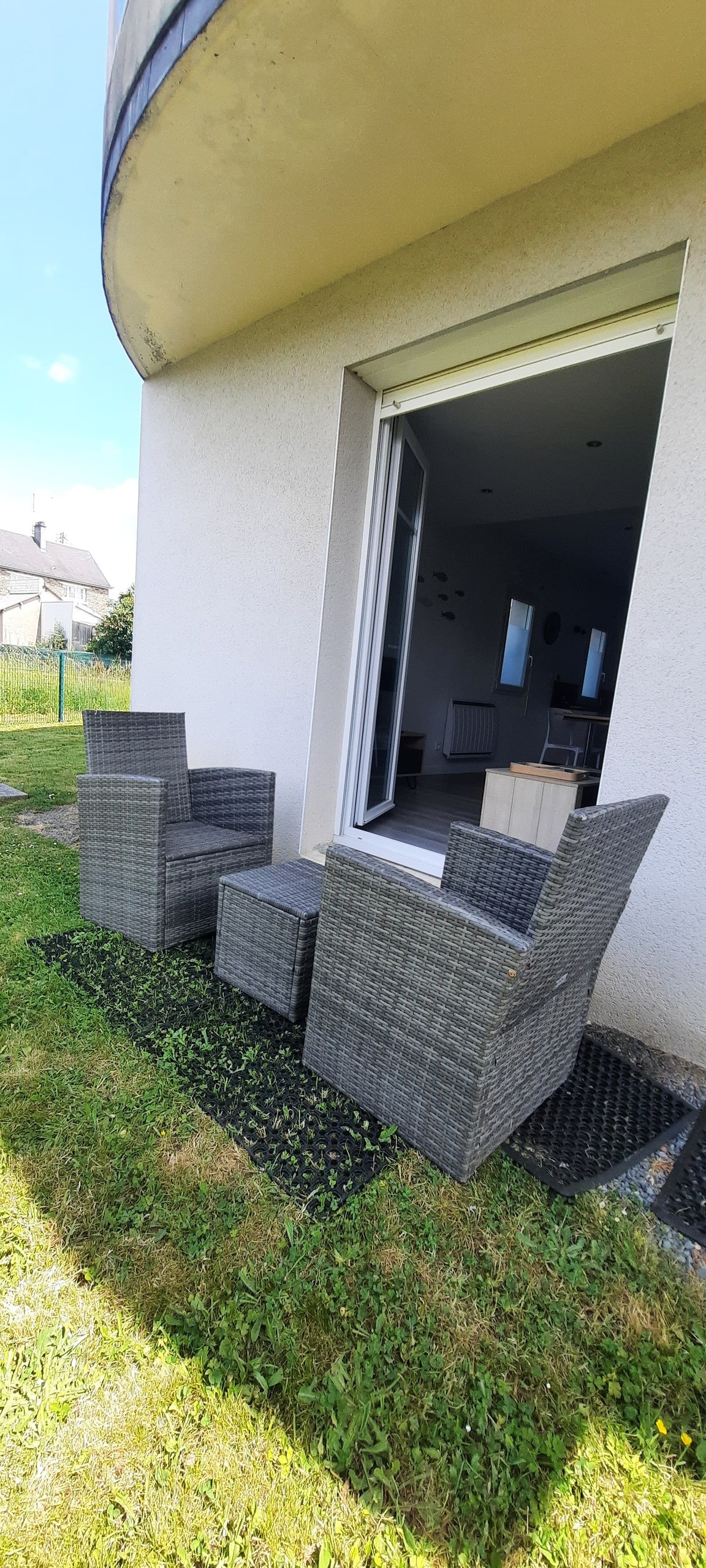Two comfortable chairs and a small table are situated on a grassy area outside. The space is accessible through sliding glass doors, providing a direct connection to the indoor living area.