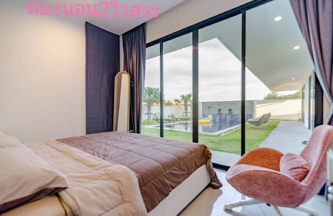 A sleeping area features a spacious bed with a neutral-toned blanket. Large glass doors provide a view of the outdoor space, revealing a grassy area and a pool. Natural light fills the room, creating an open and airy ambiance.