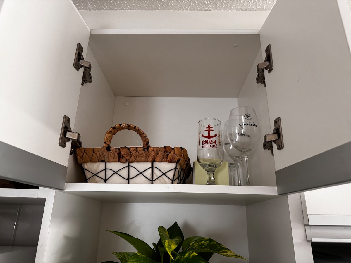 The upper kitchen cabinets reveal a neatly organized space featuring a decorative basket and two glasses. One glass bears a design with an anchor, while the other is a simple wine glass. A small green plant sits beneath the cabinets, adding a touch of greenery.