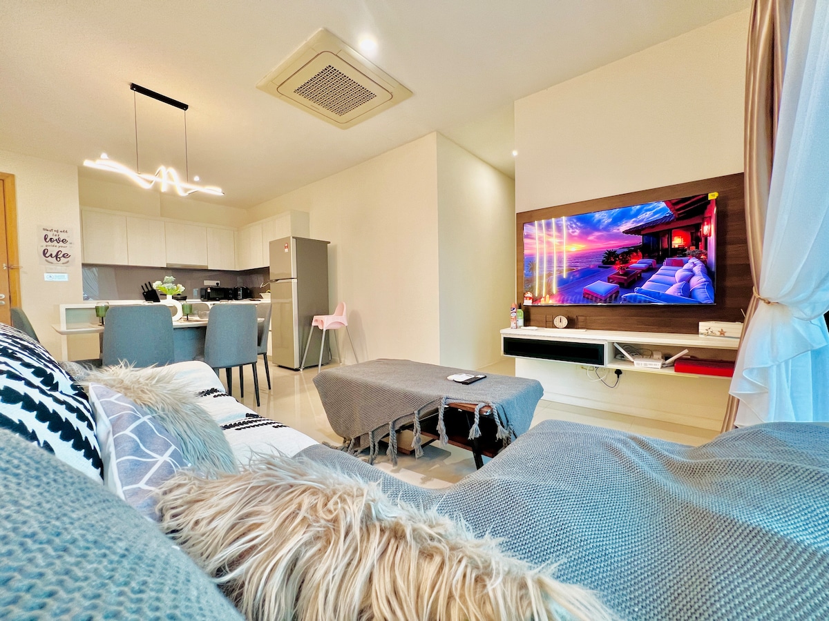 An inviting living area is featured, showcasing a comfortable couch adorned with soft pillows. A stylish coffee table sits in front, and a smart TV displays vibrant visuals. A dining space with four chairs is visible in the background, along with a fully equipped kitchen.