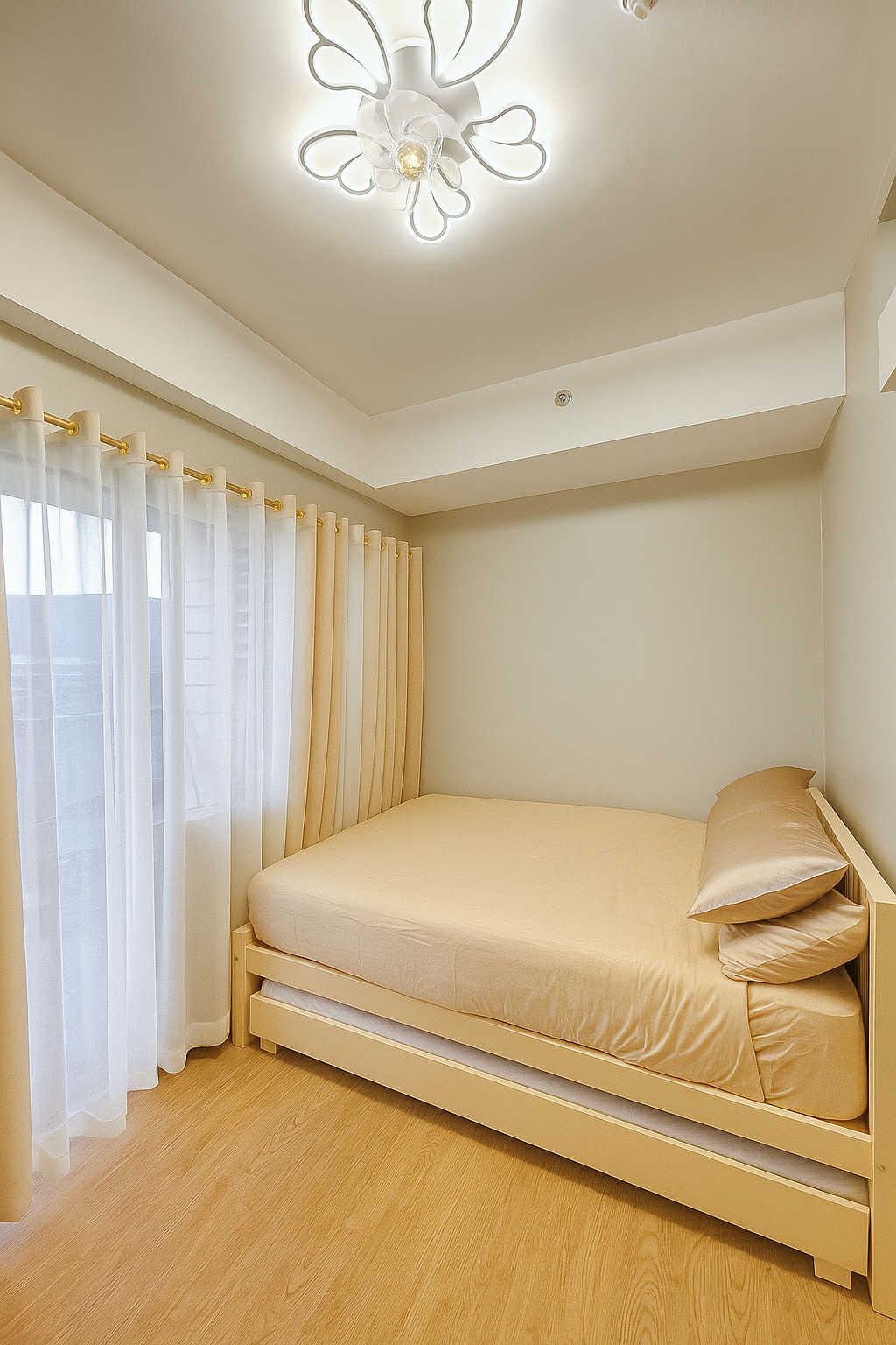 A bright bedroom showcases a spacious bed with light-colored bedding against a neutral wall. Natural light filters through sheer curtains, enhancing the calm atmosphere. The ceiling features a modern light fixture, adding subtle elegance to the room's design.