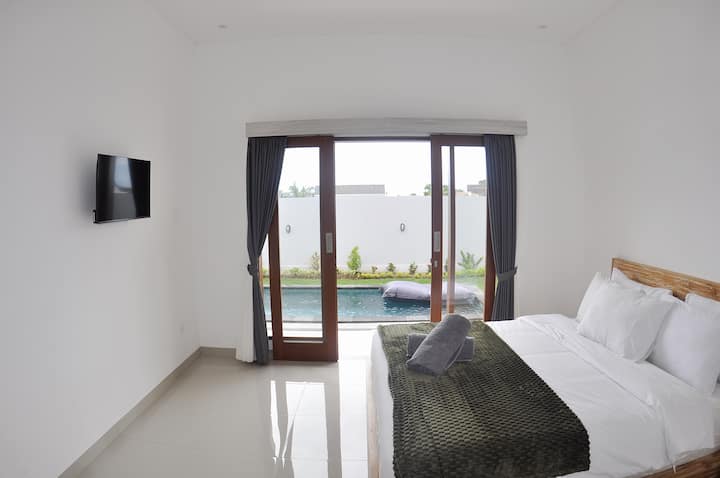 Una lujosa cama tamaño king en una habitación bellamente diseñada equipada con aire acondicionado, TV de pantalla plana y baño privado. La habitación se abre directamente a la piscina al aire libre y ofrece una conexión perfecta a una experiencia serena oasis.