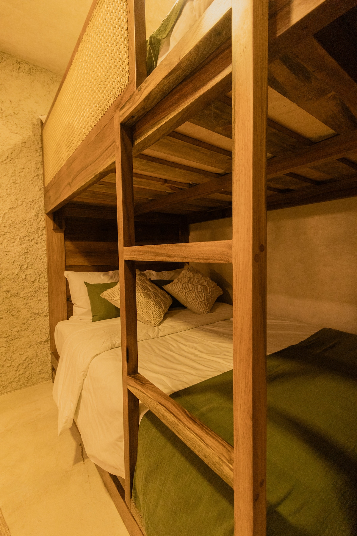 A wooden bunk bed is showcased, featuring a spacious lower level with plush bedding and decorative pillows. The upper level presents a simple, cozy sleeping space. The natural materials and warm tones enhance the room's comforting design, complemented by textured walls.