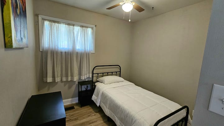 Dvojitá posteľ, nočný stolík s nabíjacími portami a zásuvkou, komoda, skriňa a stropný ventilátor.