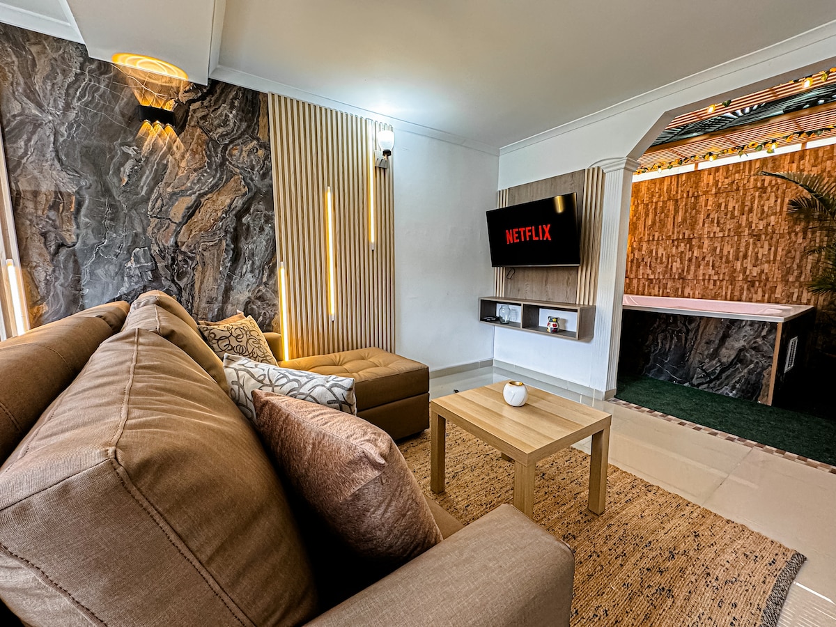 A spacious living area features a comfortable sofa and wooden coffee table, complemented by a textured stone accent wall. A wall-mounted television display shows the Netflix logo, while ambient lighting enhances the overall atmosphere. The distinct decor creates an inviting space for relaxation.