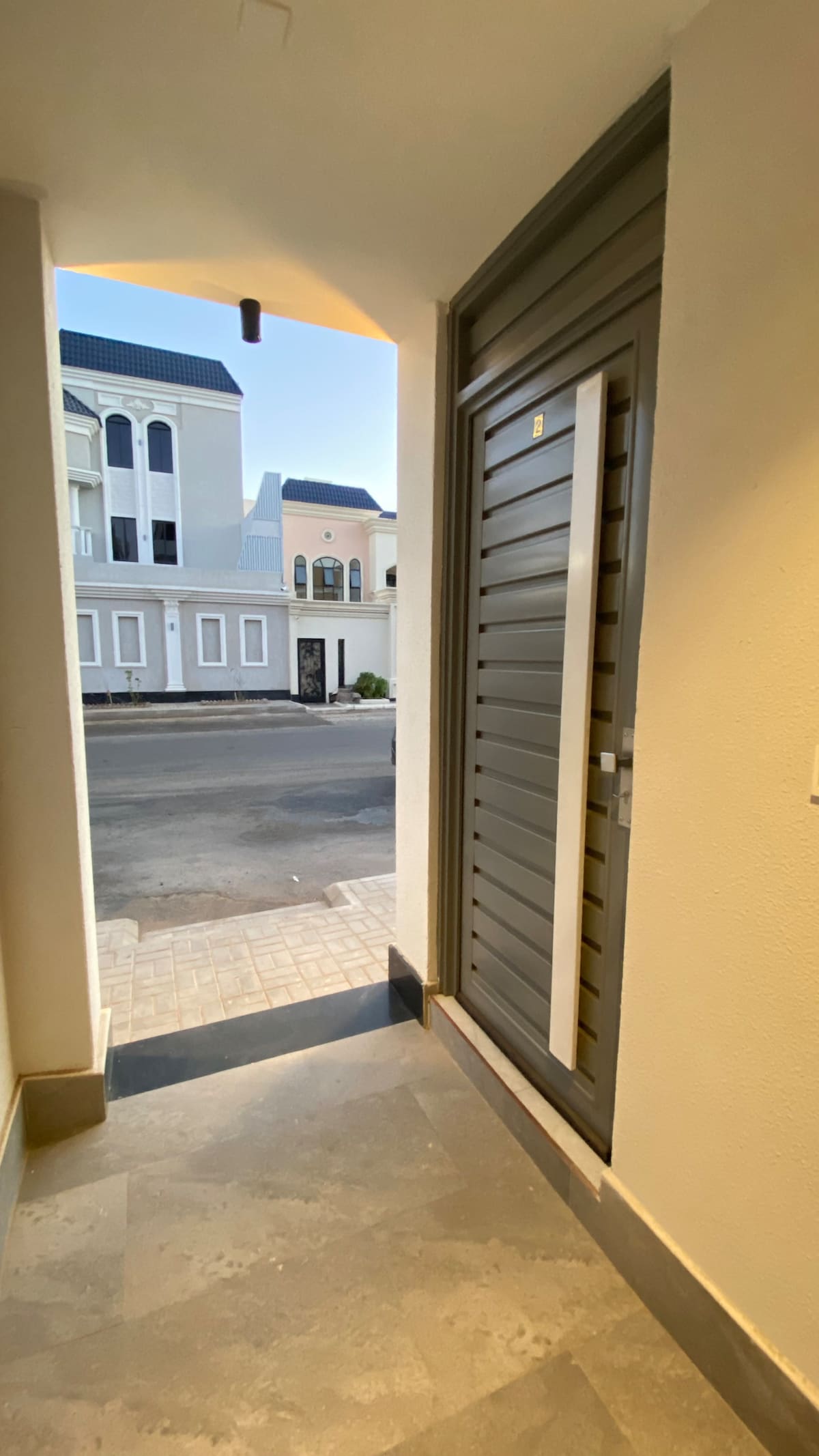 The entrance area features a modern door with horizontal slats, leading out to a charming street view. The surrounding walls are painted in a light tone, and the floor is made of tiled materials, providing an inviting access point to the room.