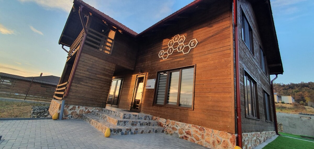 A spacious wooden exterior of the house is presented, featuring a stone accent foundation. Large windows allow natural light to fill the interior, while the entrance is highlighted by a set of steps leading up to the front door.