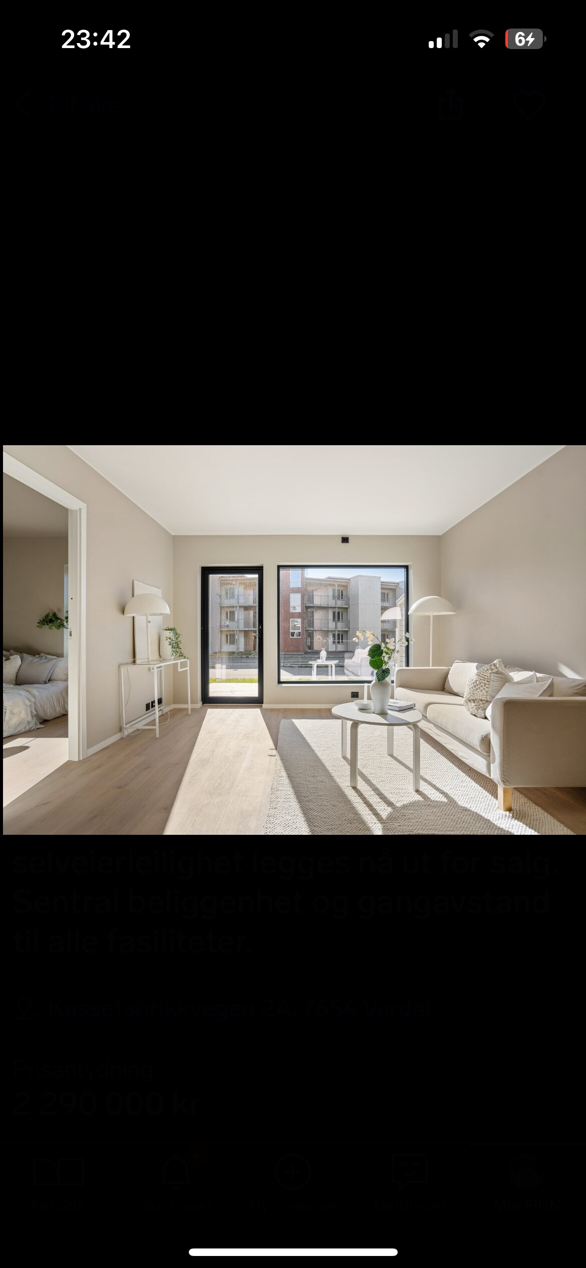 A bright living area features large glass doors that open to a balcony view. Light wooden flooring complements the light-toned walls. A minimalist white couch and a vase with greenery provide a serene ambiance, while soft natural light streams in, illuminating the space.