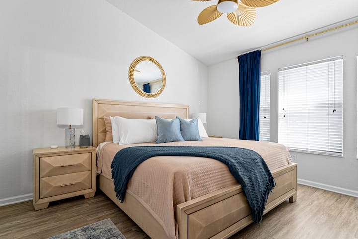 This elegant bedroom features a luxurious king-size bed with plush bedding, a chic neutral palette, and deep blue accents. A smart TV adds convenience, while natural light from large windows enhances the relaxing and inviting atmosphere.