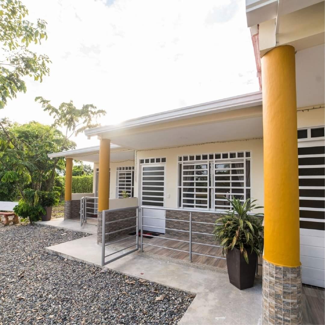 A walkway leads to a series of cottage-style accommodations, featuring large windows that allow natural light to fill each space. The exterior is complemented by vibrant columns and well-maintained greenery surrounding the area, creating an inviting entryway.
