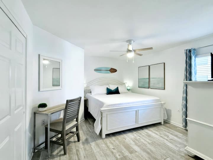 The primary bedroom is roomy and features a king bed with a new mattress, a laptop desk with chair, a closet, a large dresser, a bench and a Smart TV. 