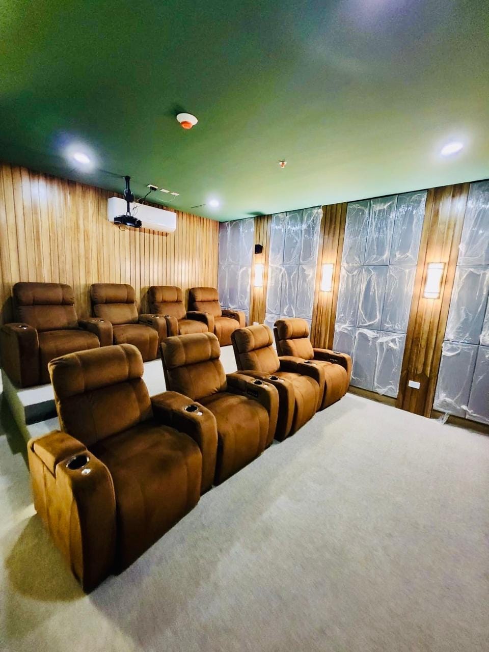 A dedicated home theater room is furnished with plush, brown reclining chairs arranged in tiered seating. Soft lighting and wood paneling create a cozy ambiance. An overhead projector is visible, while smooth gray walls provide a contemporary backdrop.