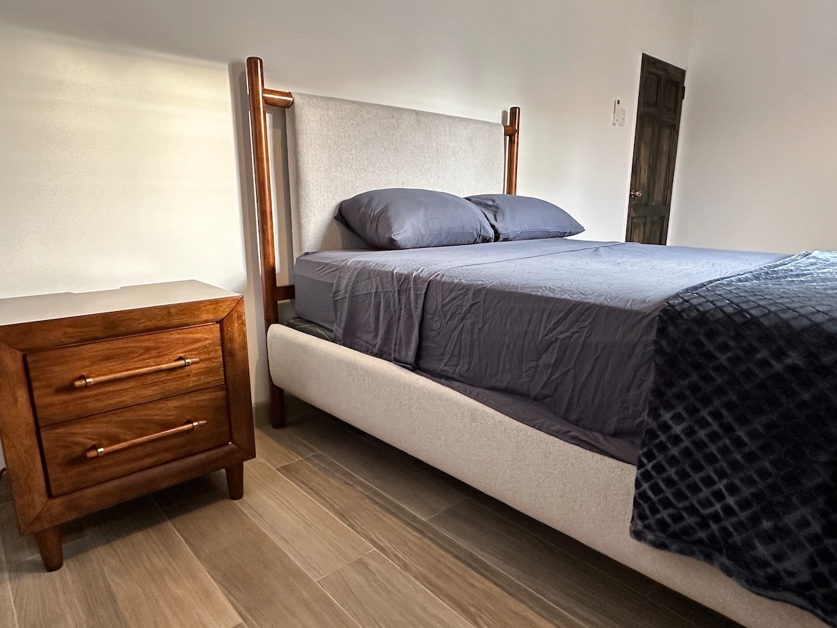 חדר שינה נוח בגודל קווין סייז עם ריצוף עץ מלוטש, מצעים מפנקים ועיצוב מינימליסטי מודרני.  מקום מפלט שקט אחרי יום של סיורים וטיולים בעיר.