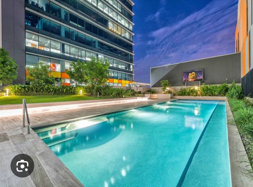 A tranquil swimming pool is framed by contemporary landscaping, featuring well-maintained greenery and modern architecture in the background. The water reflects the evening sky, enhancing the serene atmosphere of the space, which is designed for relaxation and leisurely enjoyment.