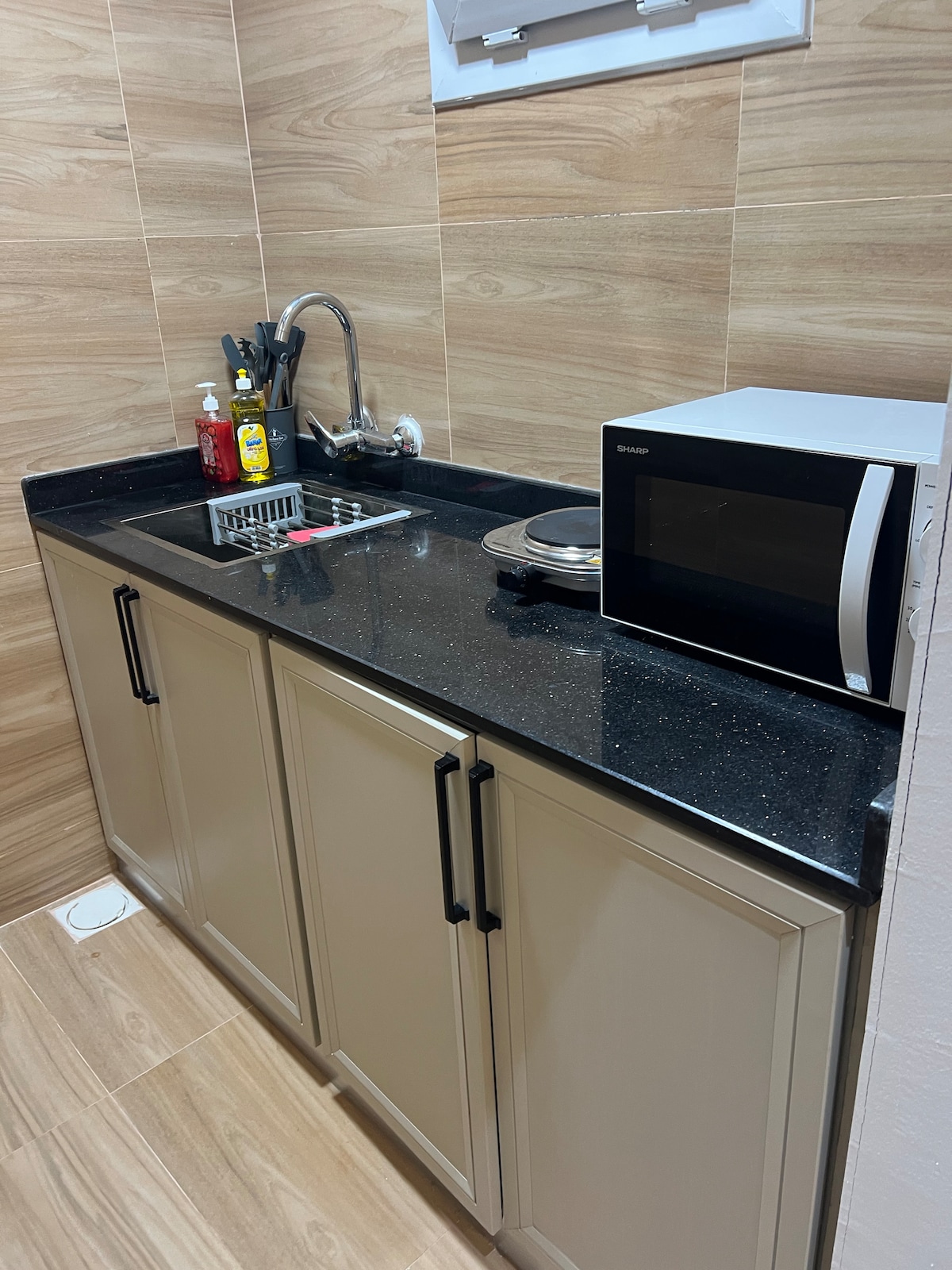 A fully equipped kitchen area is showcased, featuring dark granite countertops and light cabinetry. Essential appliances, including a microwave and a sink, are present. Utensils and condiments are neatly organized on the counter, contributing to a functional cooking space.