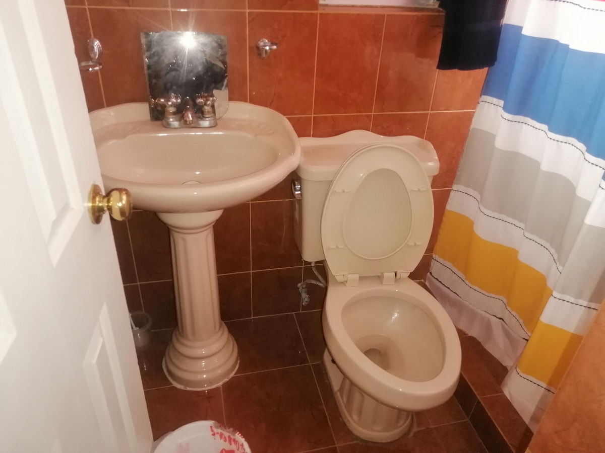 A clean bathroom is presented, featuring a pedestal sink and a toilet. The walls are adorned with decorative tiles in warm tones. A shower curtain with a colorful pattern offers privacy and complements the space.