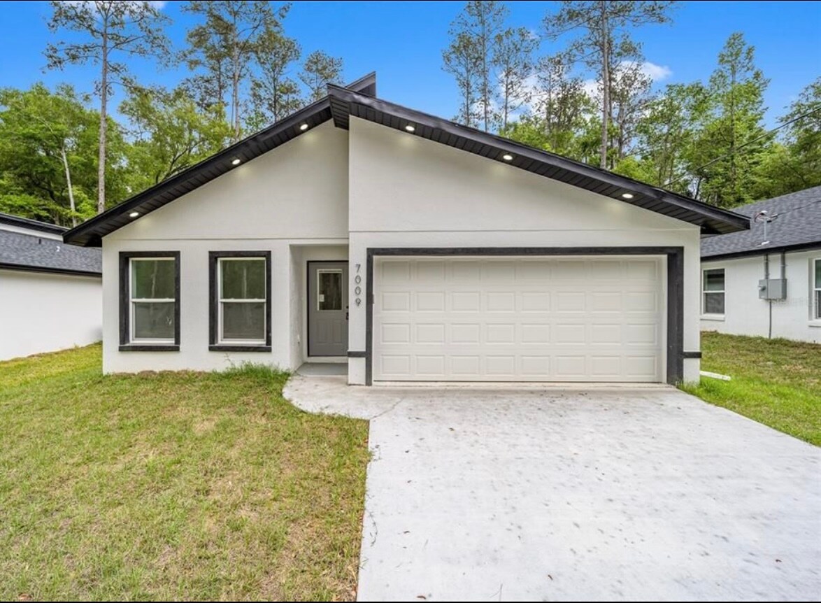 A modern single-story home is featured, showcasing a neutral-colored exterior with a sleek garage door. Two large windows on either side of the entrance provide ample natural light, while a tidy lawn enhances the welcoming appearance of the property.