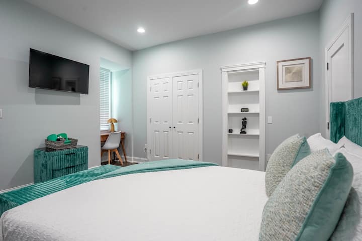 The Loft at Cedar Park Queen Bedroom: Another angle showcasing the dedicated workspace, closet storage, and wall mounted TV. A textured nightstand and soft lighting add both style and function.