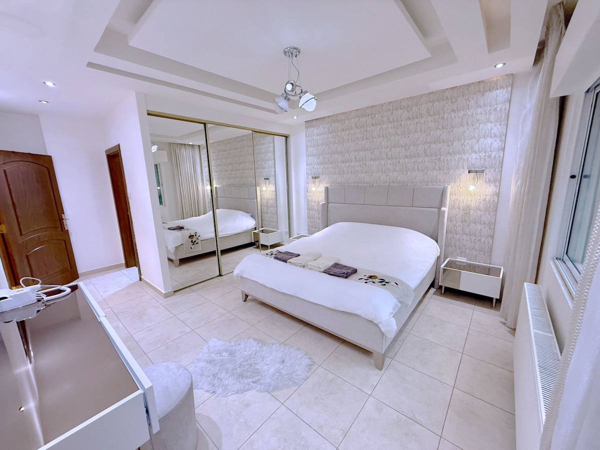 Un dormitorio principal sereno con una lujosa cama tamaño king, decoración elegante y suave iluminación ambiental; diseñado para una comodidad tranquila y de alta gama.