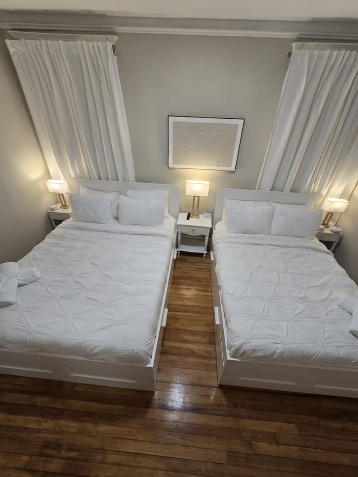 Amplio dormitorio con una cama tamaño queen y una cama de tamaño completo. Incluye TV, armario, espejo de cuerpo entero, lámparas de noche, máquina de sonido para dormir mejor y cortinas oscuras para mayor comodidad. Perfecto para familias o amigos que viajan juntos.