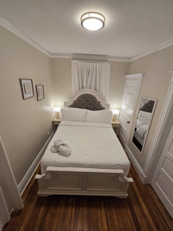 Cómodo dormitorio con cama tamaño queen, sábanas suaves y lámparas de cabecera para un ambiente relajante. Incluye un televisor para tu entretenimiento, espacio en el armario y un espejo de cuerpo entero. Un espacio acogedor y tranquilo para descansar después de un largo día.