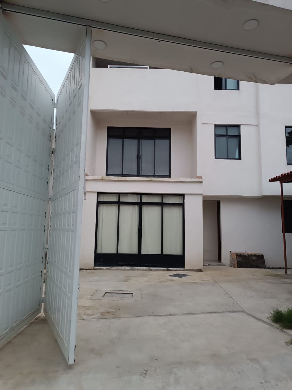 The exterior view reveals a modern, two-story building with large glass doors that open onto a patio. A spacious entryway is framed by high walls, and the surrounding area features concrete flooring and simple landscaping.