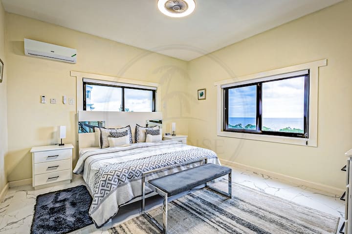 Táto štýlová spálňa je svetlá a vzdušná a môže sa pochváliť pruhovanou posteľnou bielizňou, dekoratívnymi vankúšmi a dvojitými oknami, ktoré zapĺňajú priestor prirodzeným svetlom. Elegantná klimatizačná jednotka a moderný nábytok dodávajú pohodlie a šarm.
