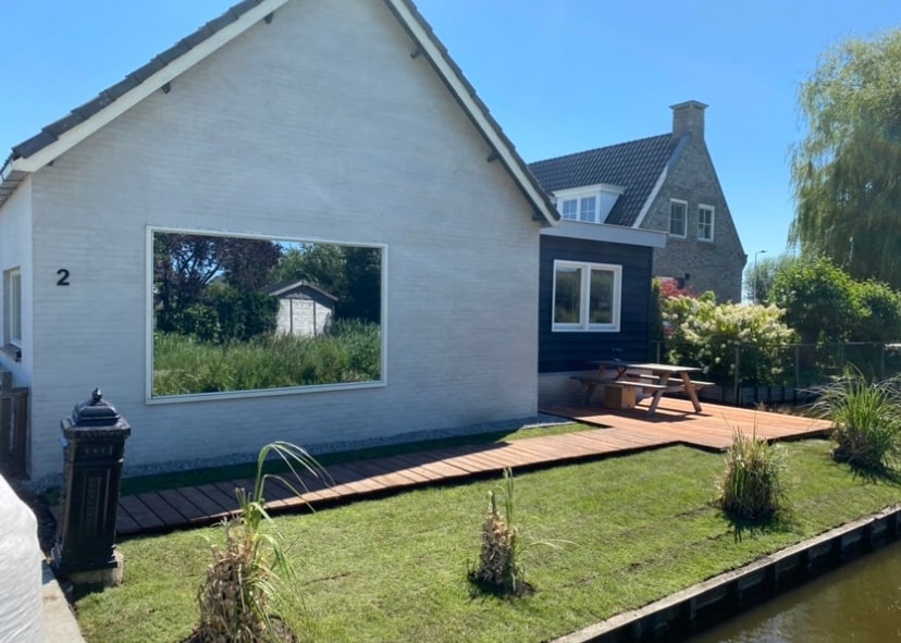 The exterior of the family-friendly home is shown, featuring a well-maintained garden and a wooden pathway leading to a picnic table. A large window provides a clear view of the surrounding greenery, enhancing the connection to nature.