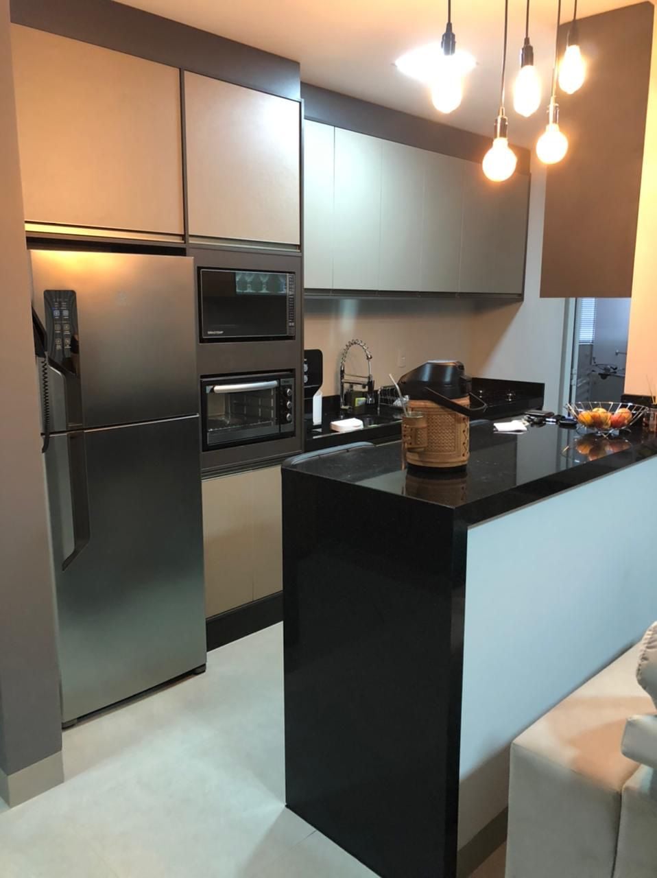 A modern kitchen features sleek cabinetry with a mix of light and dark tones. Stainless steel appliances include a refrigerator and built-in oven. A black countertop complements the space, while pendant lights provide illumination above the bar area, enhancing functionality and style.