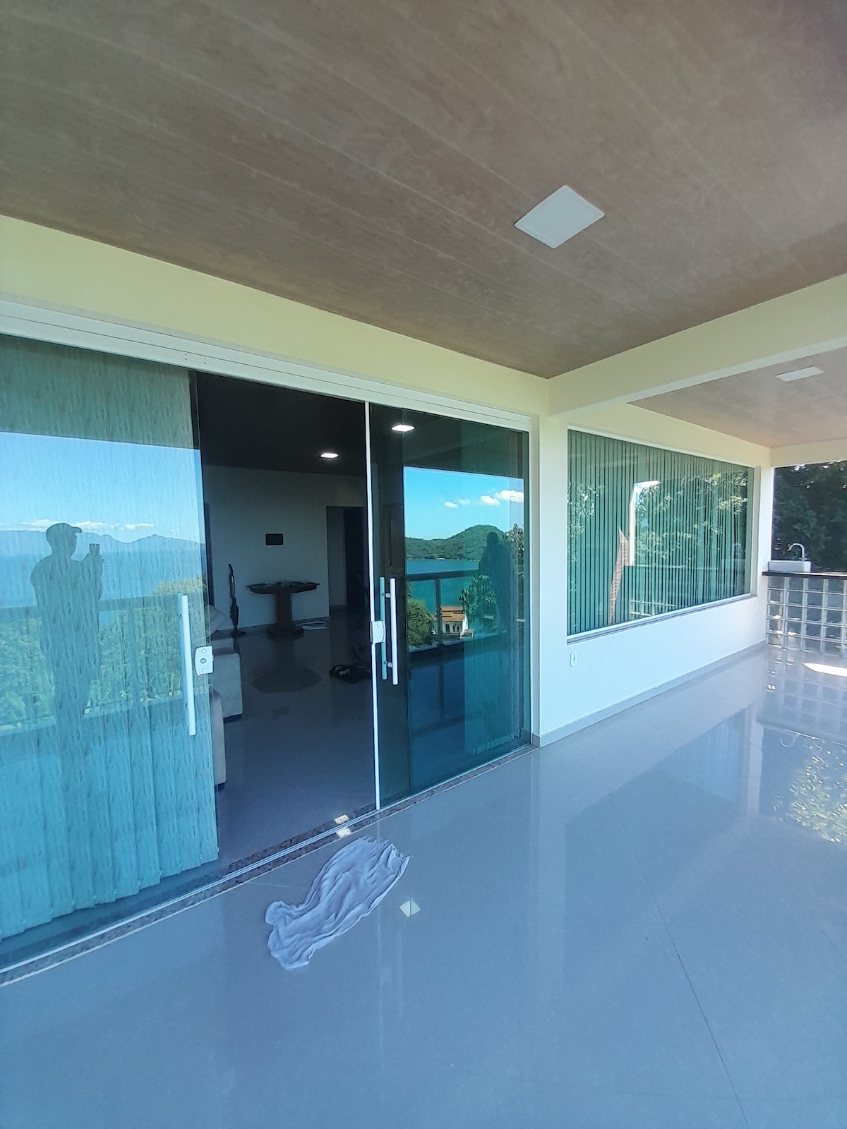 Large sliding glass doors open to reveal a bright, airy space. Smooth, polished flooring reflects natural light. A view of the surrounding landscape is accessible through the transparent glass, enhancing the connection with nature. A soft curtain is drawn to one side, allowing for ample sunlight.