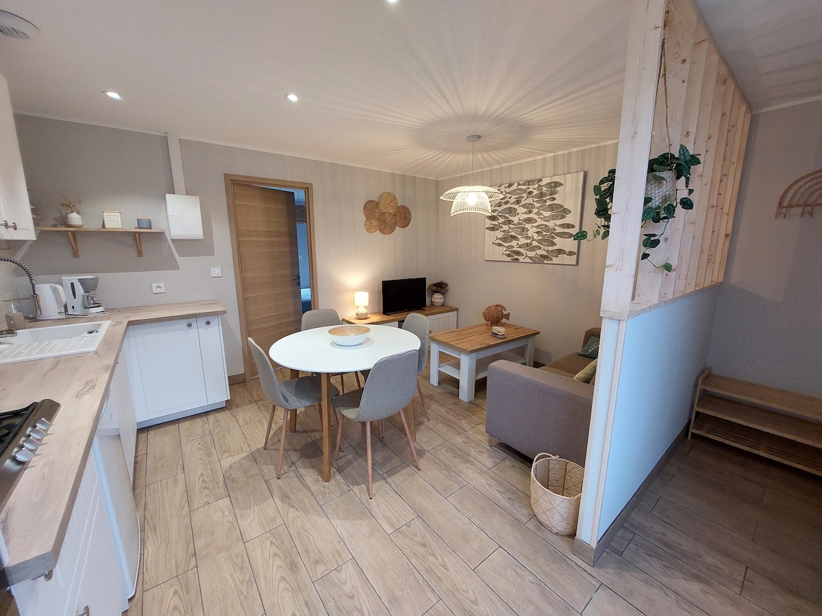 The renovated living area displays a simple and modern design, featuring a round dining table with four chairs beside a comfortable seating arrangement. A television is positioned near a decorative wall art depicting fish, while a light fixture hangs from the ceiling, creating a welcoming atmosphere.