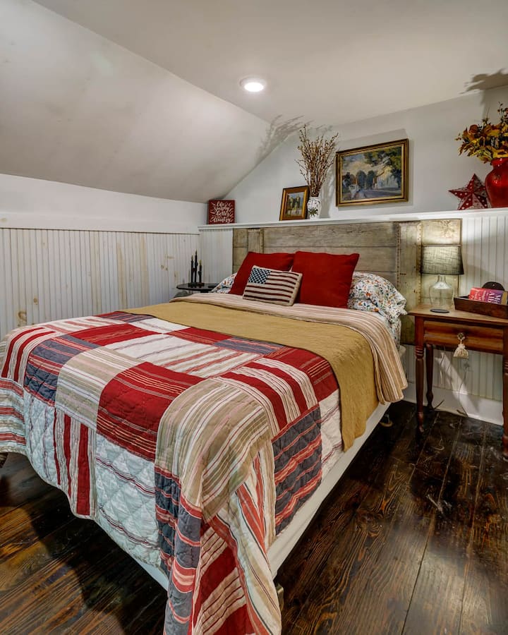 Rest easy in a queen bedroom with a reclaimed-wood headboard, soft Pottery Barn quilt, and cozy historic character.