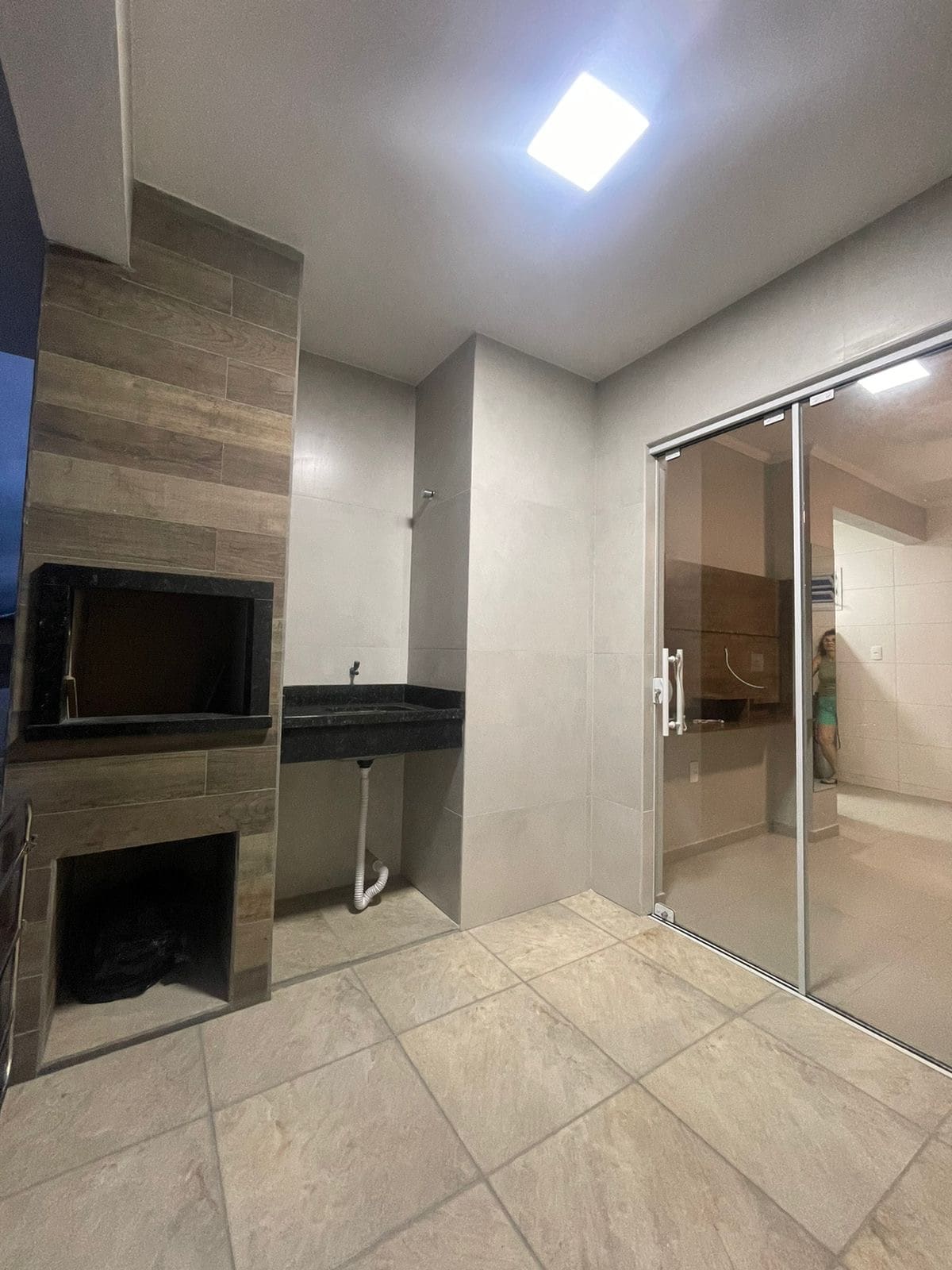 A clean and modern space is shown, featuring a black granite countertop and a built-in grill for outdoor cooking. Sliding glass doors lead to a well-lit area, and the tiled floor adds a neutral tone to the room.