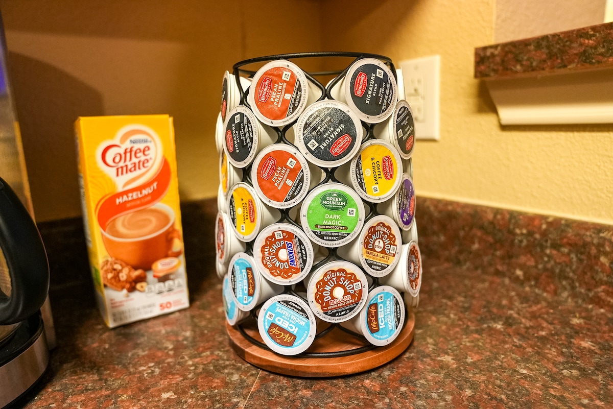 A variety of coffee pods is organized in a cylindrical holder on the kitchen countertop. A carton of hazelnut creamer is positioned nearby, providing additional options for coffee preparation.