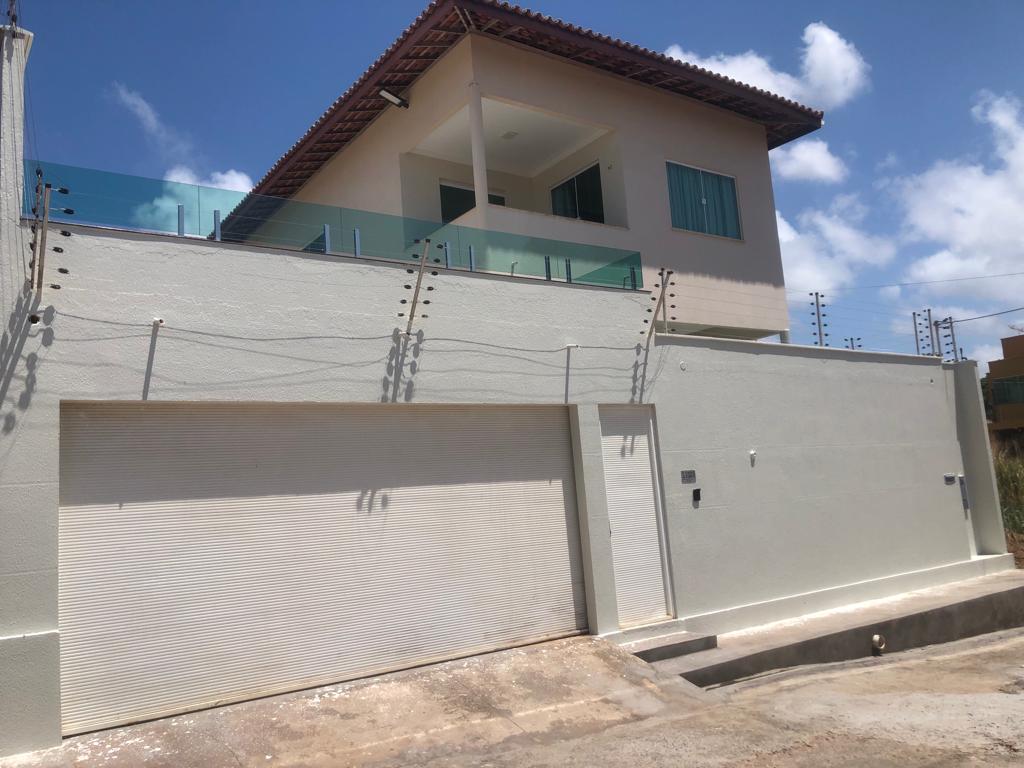 The modern building features a minimalist exterior with a light-colored facade. A spacious balcony with glass railing is visible on the upper level. A garage door is located at ground level, showcasing a clean and well-maintained environment.