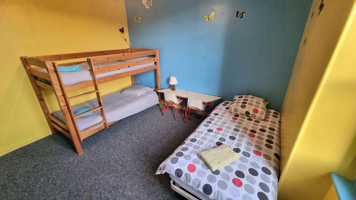 Dhoma e dytë e gjumit me tre krevate tek dhe një tavolinë pune.