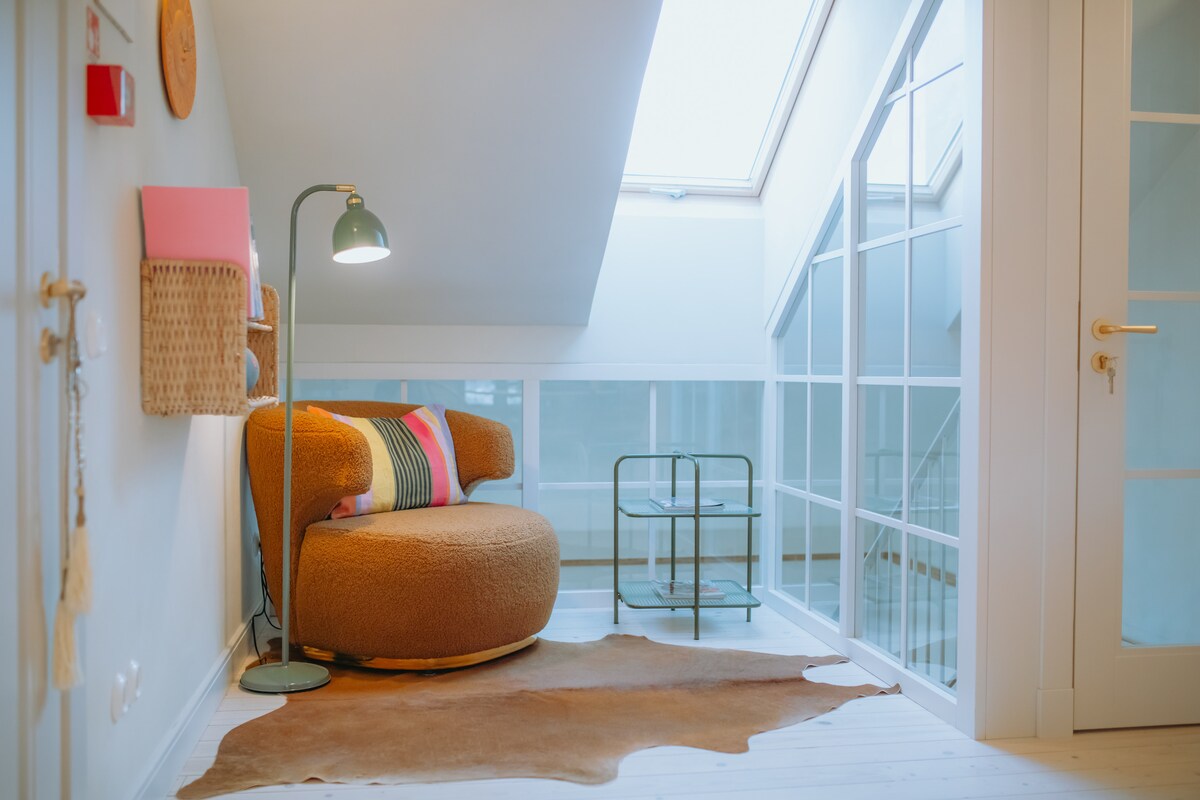 A cozy seating area features a plush, round armchair adorned with colorful cushions. A sleek floor lamp provides gentle lighting. A stylish glass table is positioned nearby, alongside a soft cowhide rug, creating an inviting corner that invites relaxation.