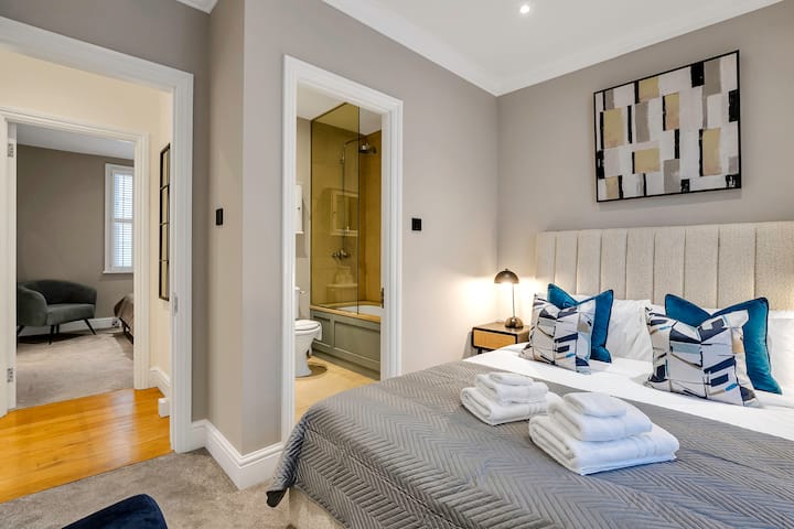 Dormitorio moderno con baño privado, ropa de cama acogedora y decoración elegante.
