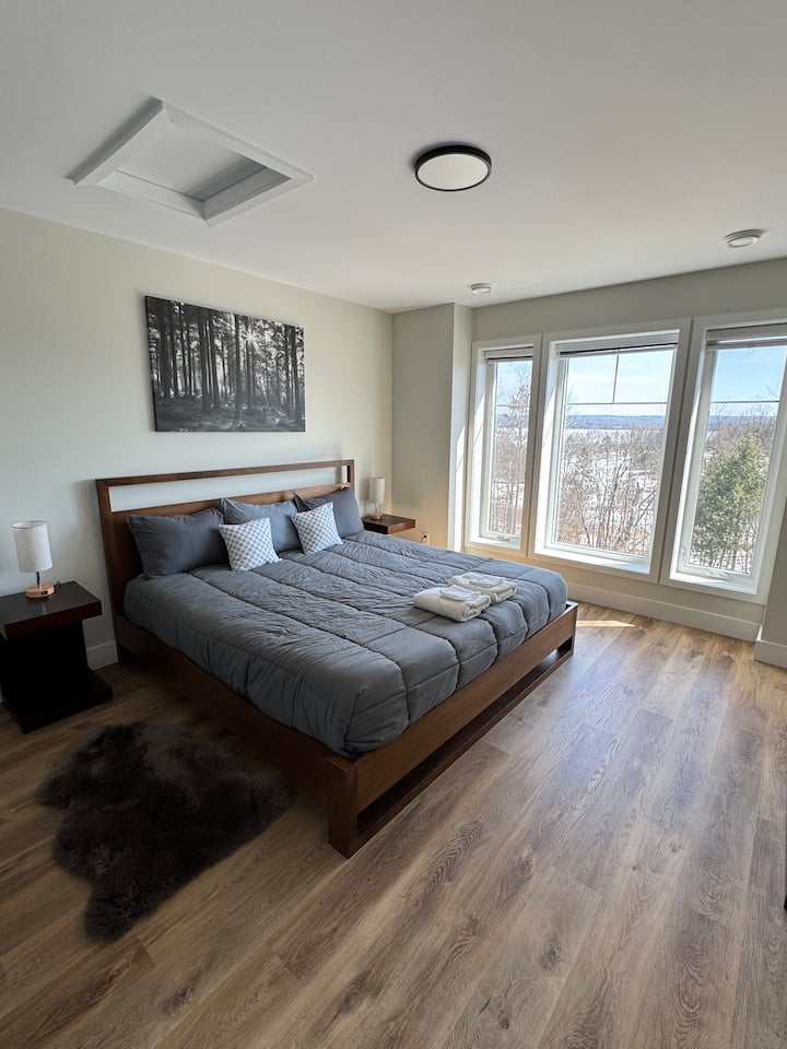 Chambre principale spacieuse avec lit King, salle de bain attenante et vue magnifique sur le lac et les arbres