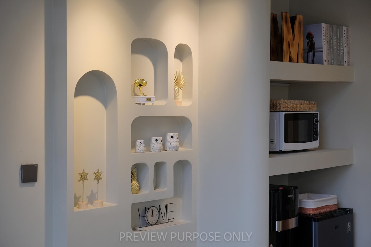 גומחות קיר אמנותיות עם קשתות ייחודיות וצורות אורגניות משמשות כמוקד יצירתי. תאורה יפה עם זרקורים חמים משולבים, הם מציגים קישוטי זהב ועיצוב מינימליסטי כנגד מרקם לבנים נקי, בצבע לבן-שמנת.