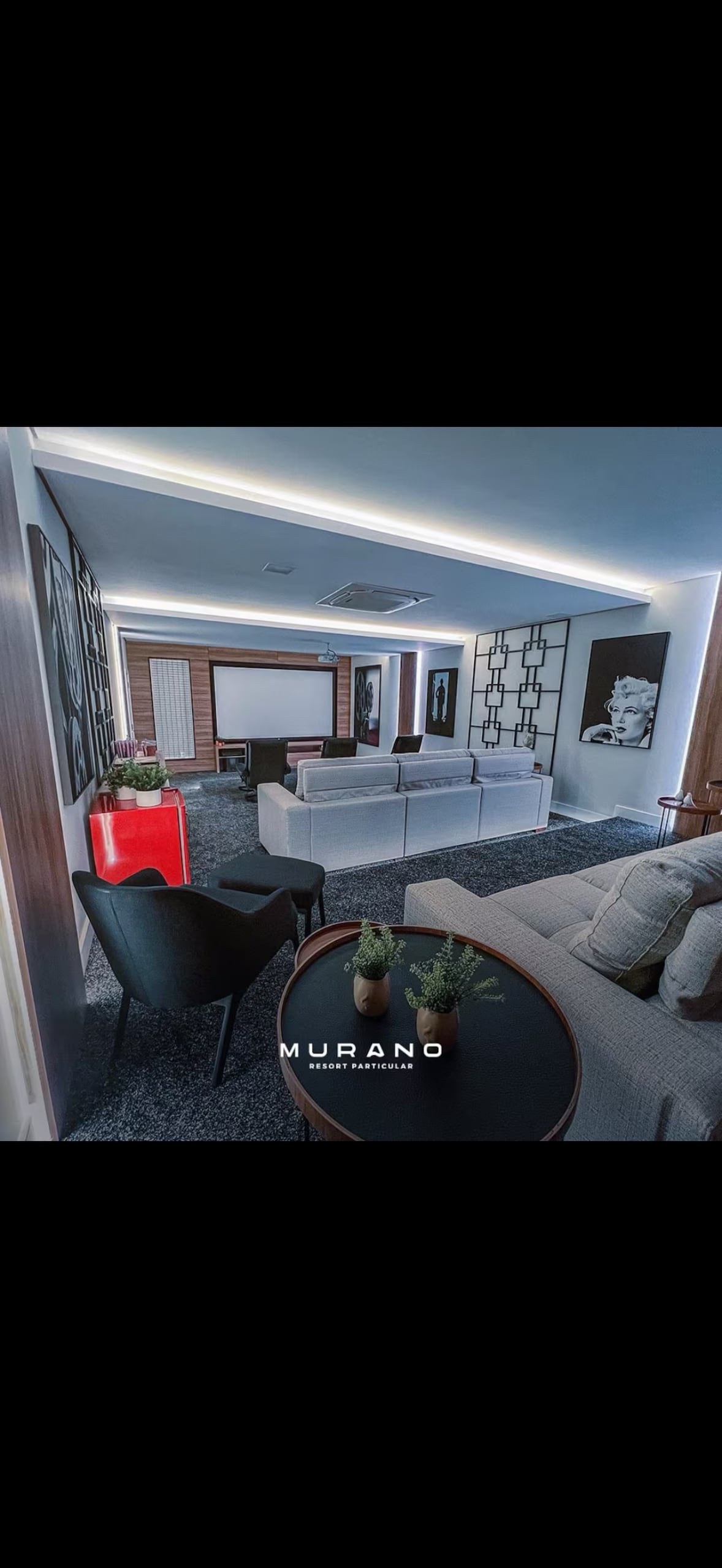 A modern living area features a sleek sofa and minimalist decor, complemented by a low coffee table set with decorative items. A large television is mounted on the wall opposite, while ambient lighting highlights the room's clean lines and contemporary style.