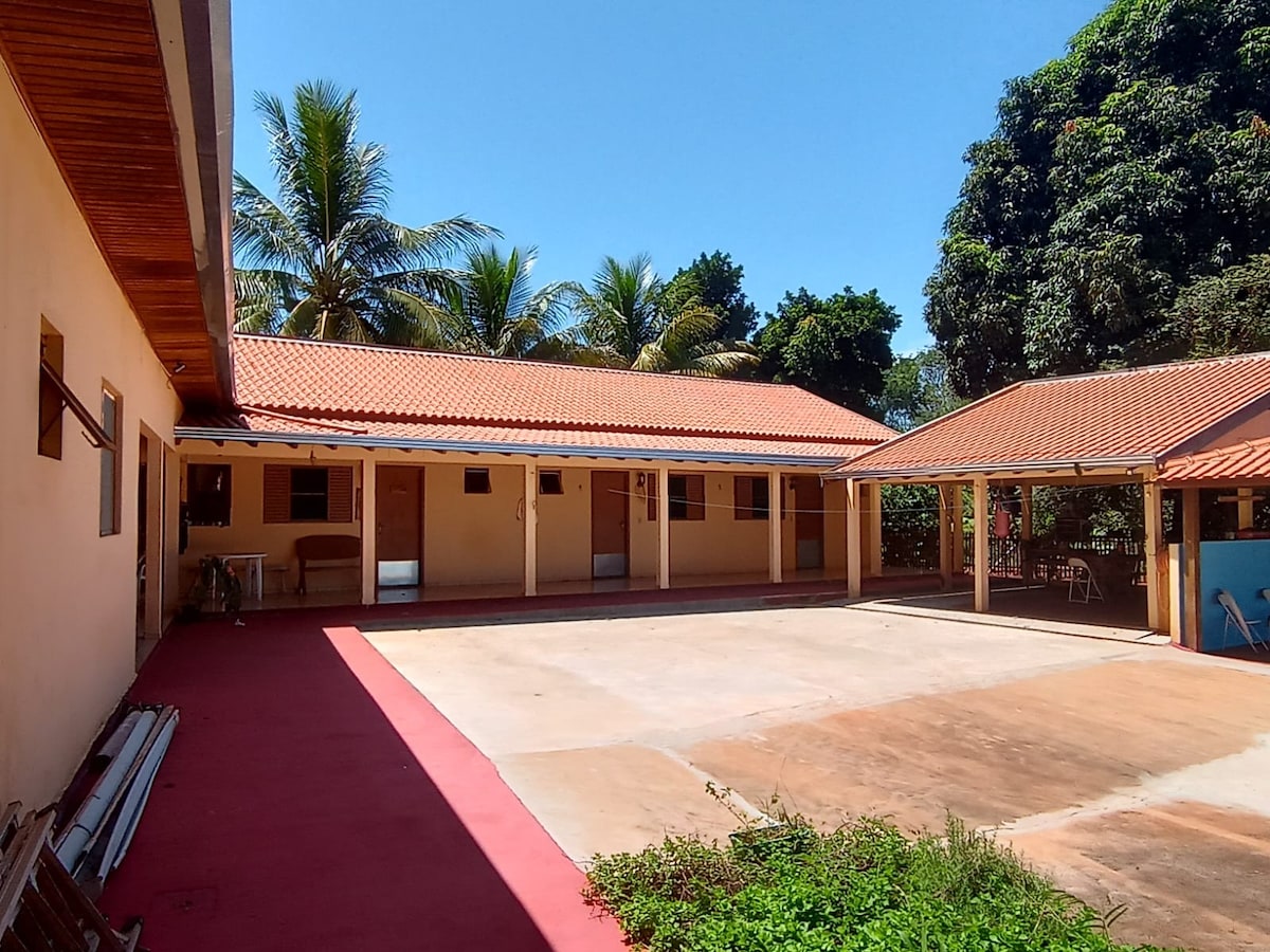 A spacious courtyard is enclosed by several single-story buildings with terracotta roofs. Palm trees provide shade, enhancing the outdoor ambiance. A concrete area offers ample space for gatherings, surrounded by well-maintained greenery.