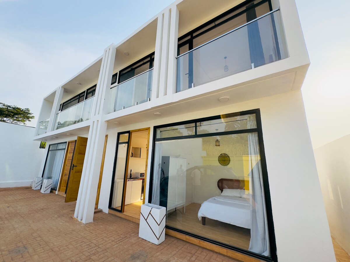 The exterior of the penthouse showcases a modern two-story structure with large glass doors and balconies. The clean lines and white facade create a fresh look, while the outdoor area features tiled flooring and planters, enhancing the inviting entrance to the living space.